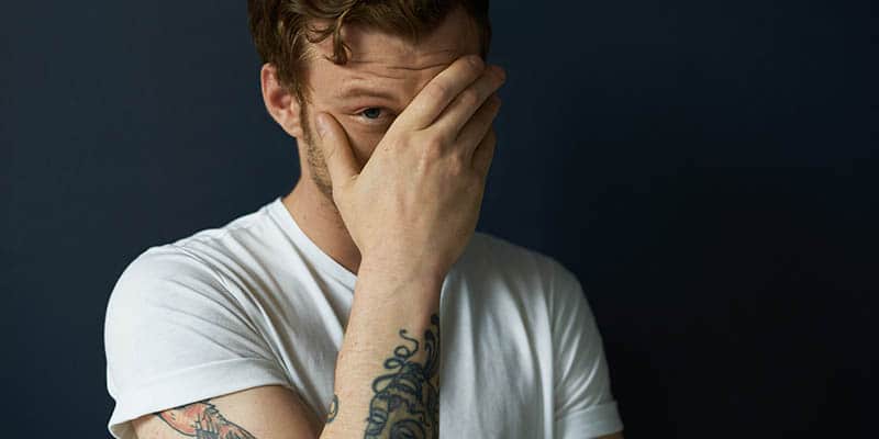 Embarrassed man with tattoos and white shirt