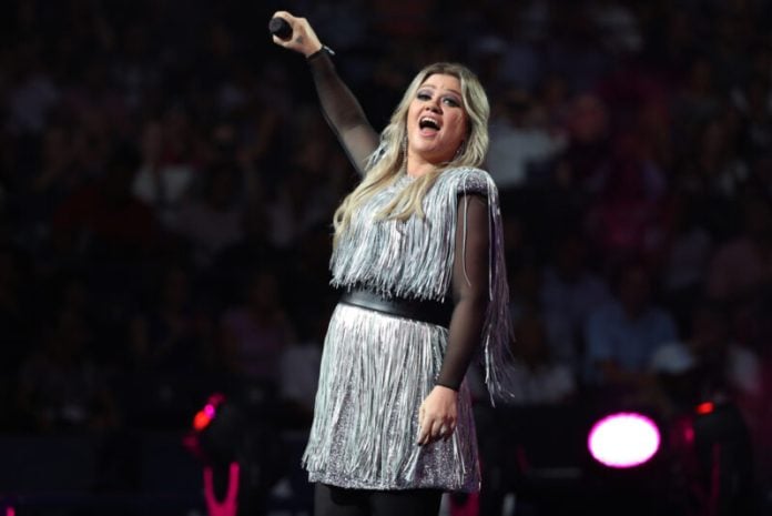 kelly clarkson in a silver fringe dress holding up a microphone