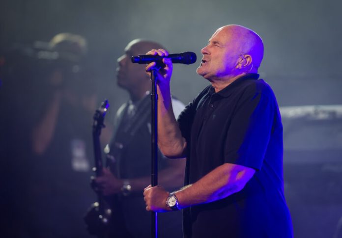 phil collins' net worth phil collins songs. phil collins on stage singing into a microphone