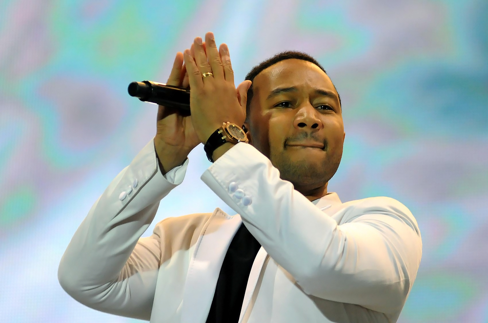 john legend on stage clapping while holding a microphone