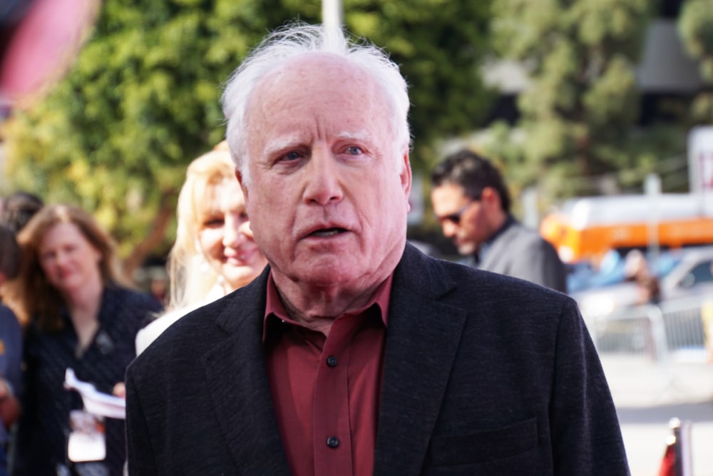 richard dreyfuss in a dark suit coat and red shirt outside