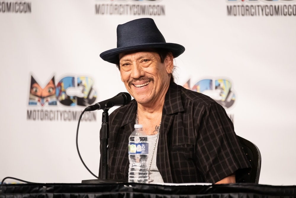 danny trejo in a hat giving an interview