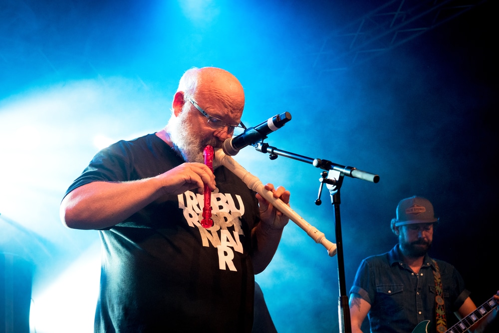 kyle gass's net worth Kyle Gass, stocky grey bearded man in a black shirt, playing two recorders.